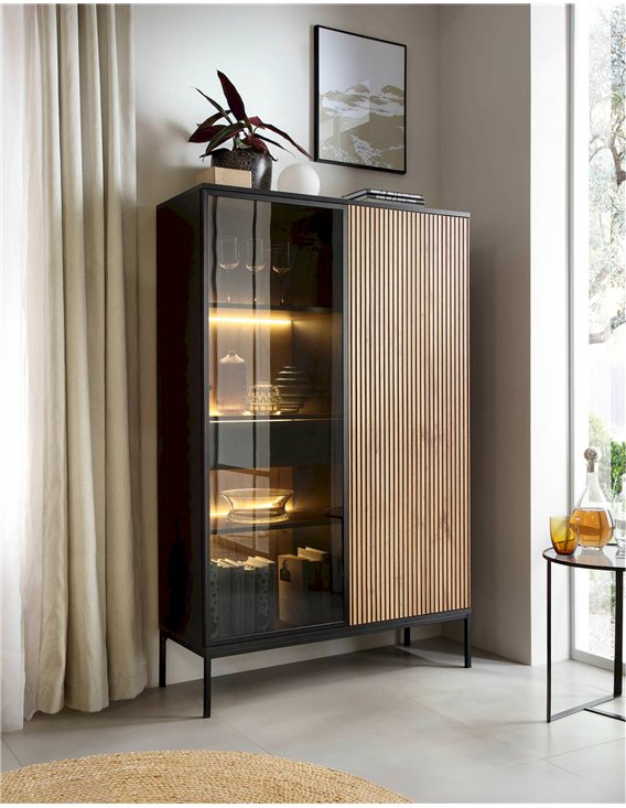 Vitrine haute noire et bois clair dans un coin de pièce, avec verres et assiettes