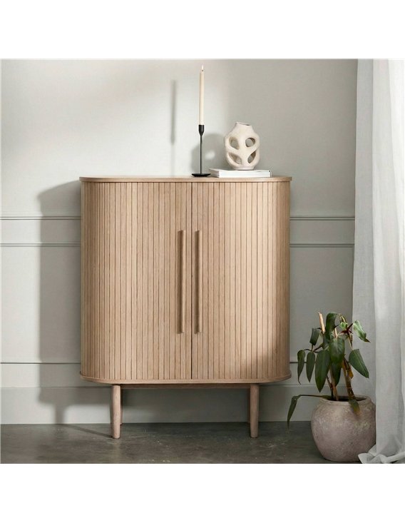 Commode haute rainurée claire dans un intérieur, avec bougie et plante en pot