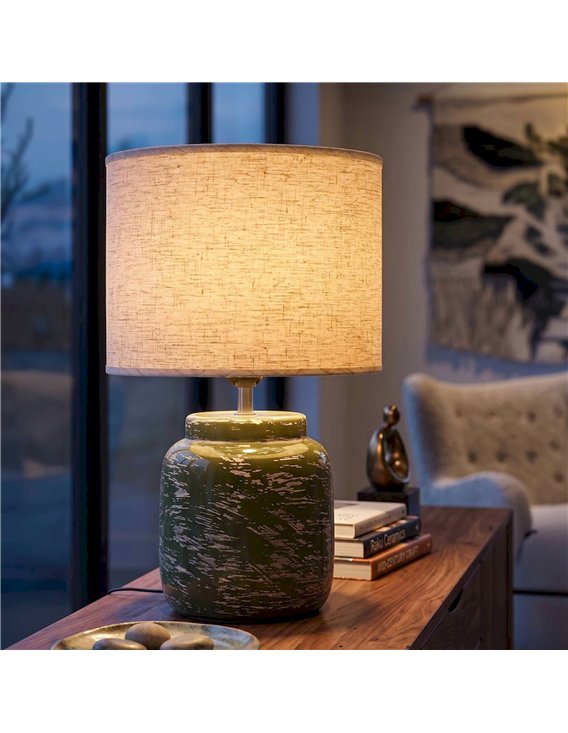 Lampe à poser verte allumée sur un meuble en bois devant une baie vitrée