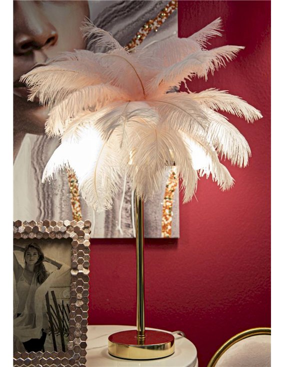 Lampe à poser plumeuse rose allumée devant un mur rouge et un cadre
