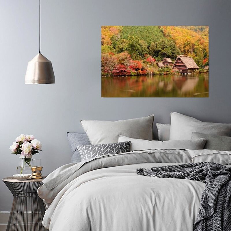 Tableau le paysage côtier accroché au-dessus d'un lit, chambre aux draps gris et lampe suspendue